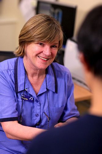 Smiling nurse in blue scrubs with a stethoscope talking to a patient