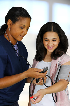 Black nurse in navy scrubs taking a smiling young patient's blood pressure