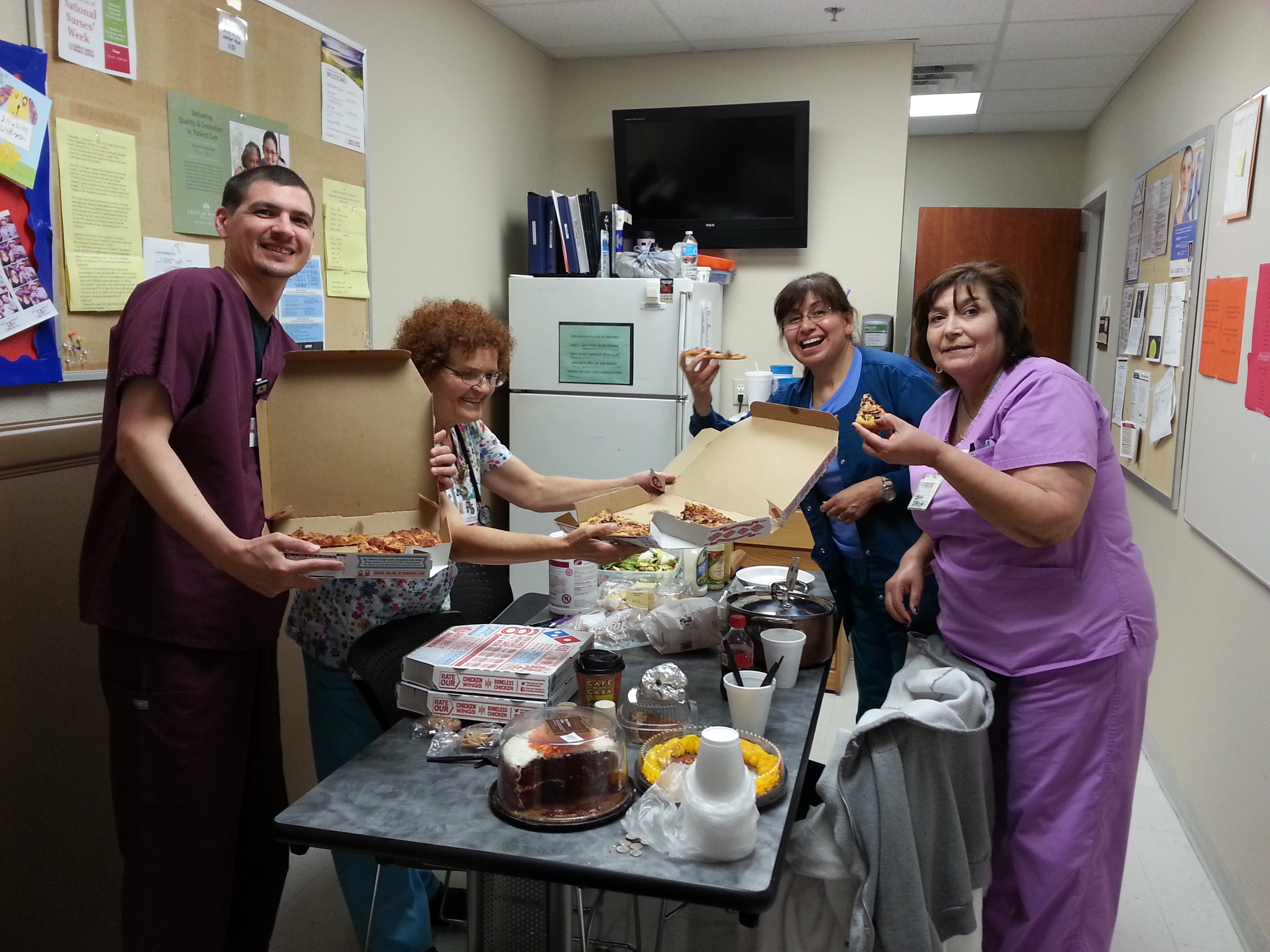 Four staff members gathered around a break room table of pizza and snacks