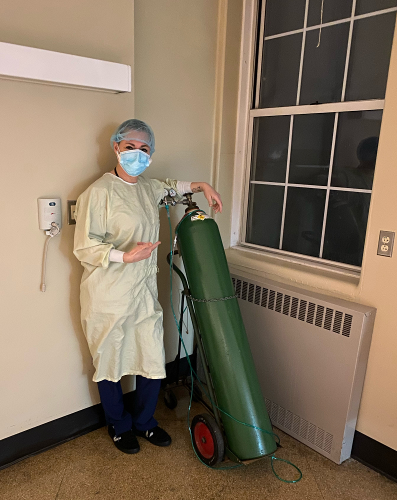 Monica Segrist in full PPE standing beside a large green oxygen cylinder