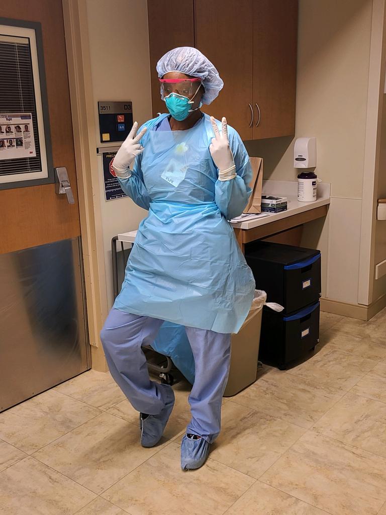Tatenda Bomba in a blue isolation gown, cap and mask, giving a thumbs up