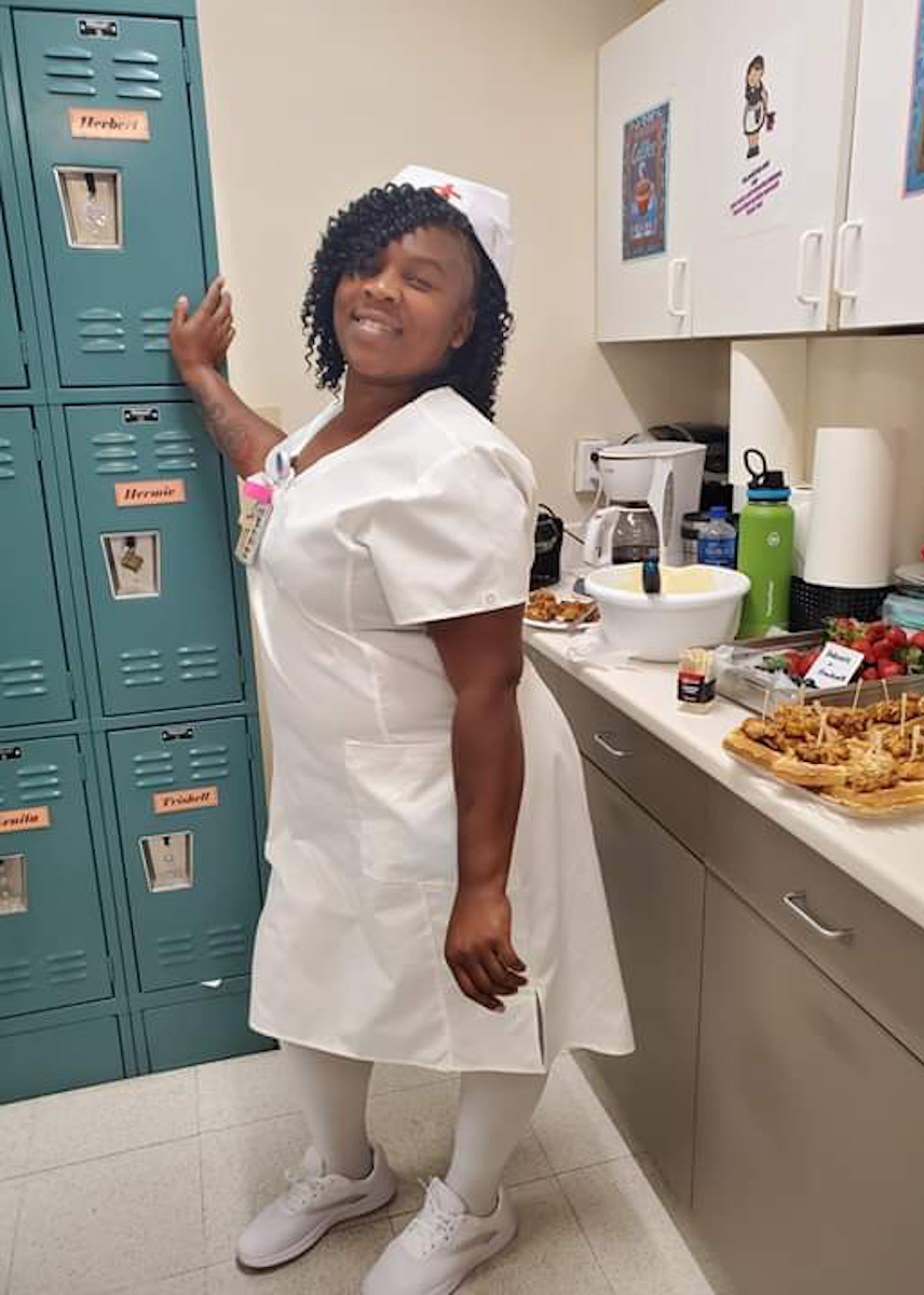 Trishell Gladney posing in a vintage white nurse uniform and cap beside lockers