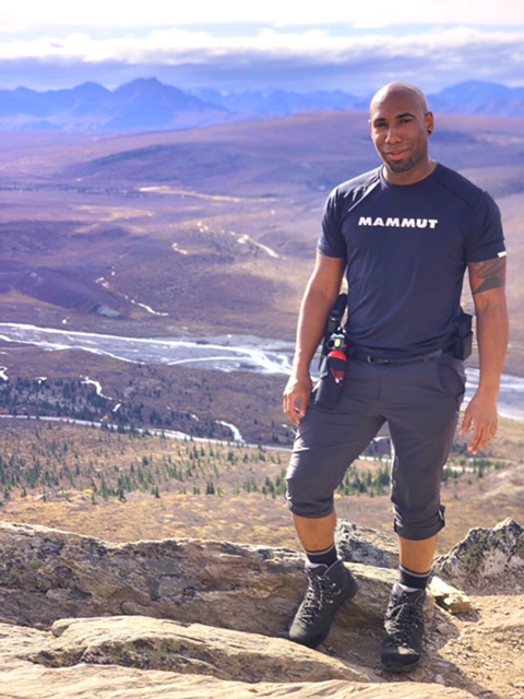 Hiker in shorts and daypack standing on a clifftop over tundra