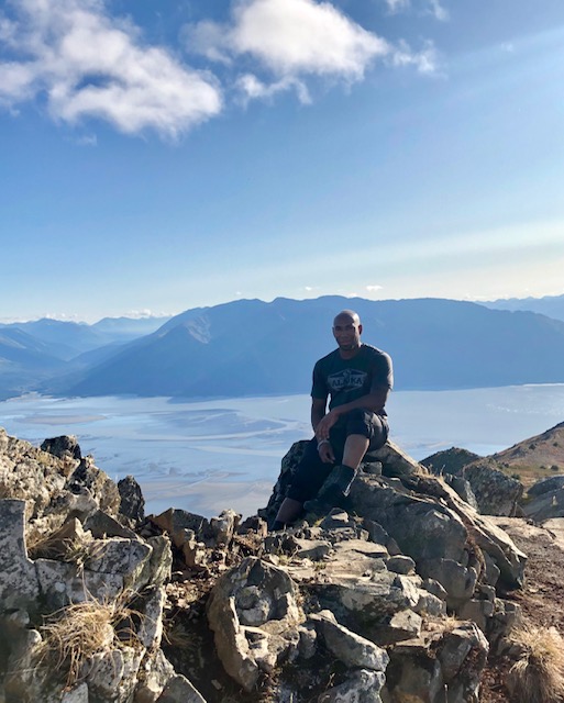 Hiker resting on a rocky ridge high above a sunlit fjord