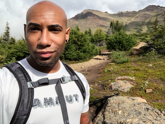 Smiling hiker with backpack on an alpine trail below a rocky peak
