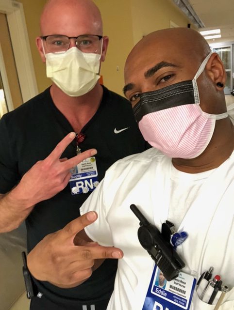 Two masked nurses in scrubs pose together in a hospital corridor