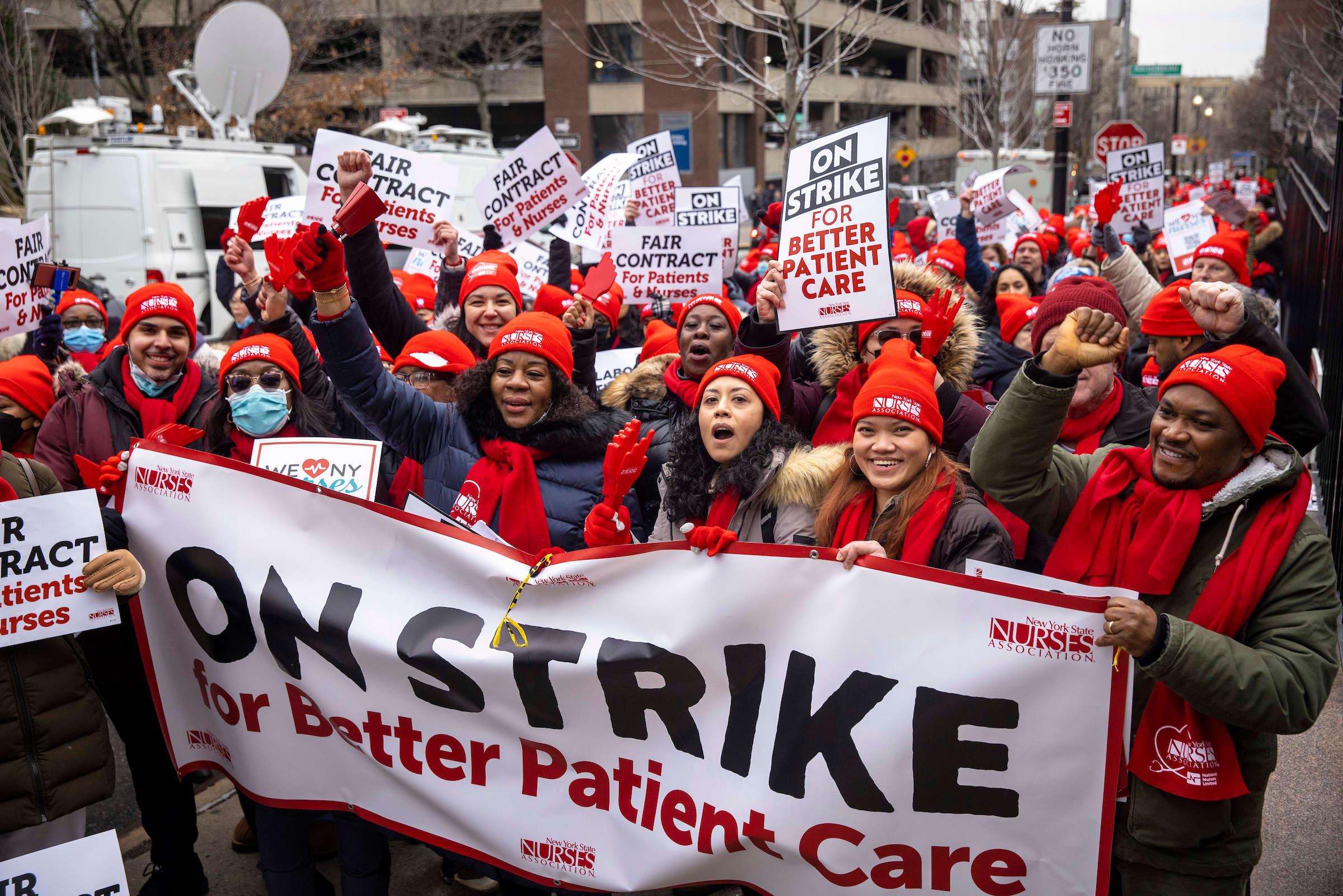Crowd of nurses in red hats behind a banner reading On Strike for Better Patient Care