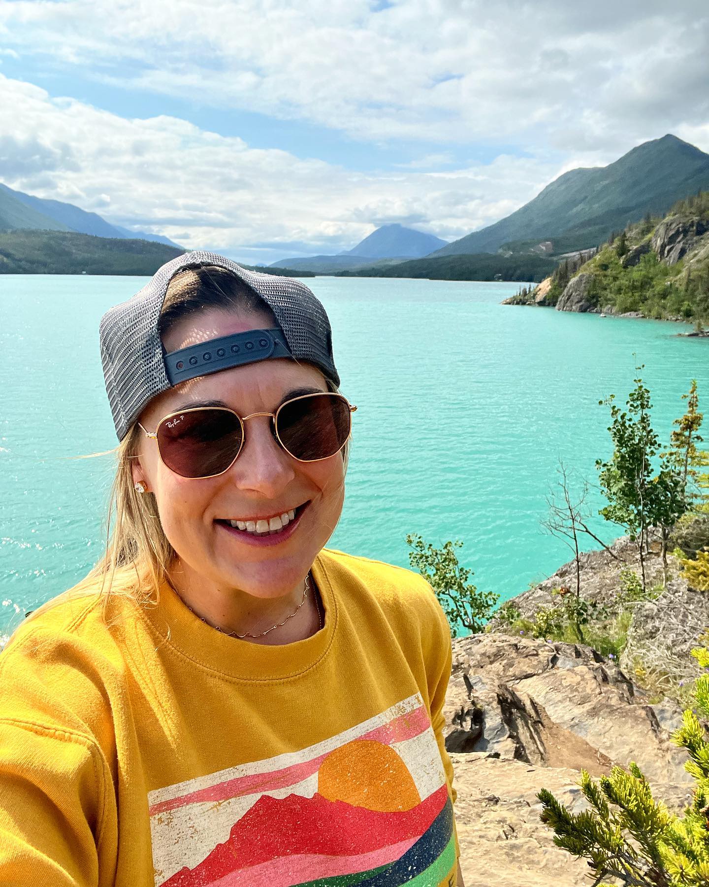 Smiling traveler in a backwards cap and sunglasses, selfie beside a turquoise mountain lake