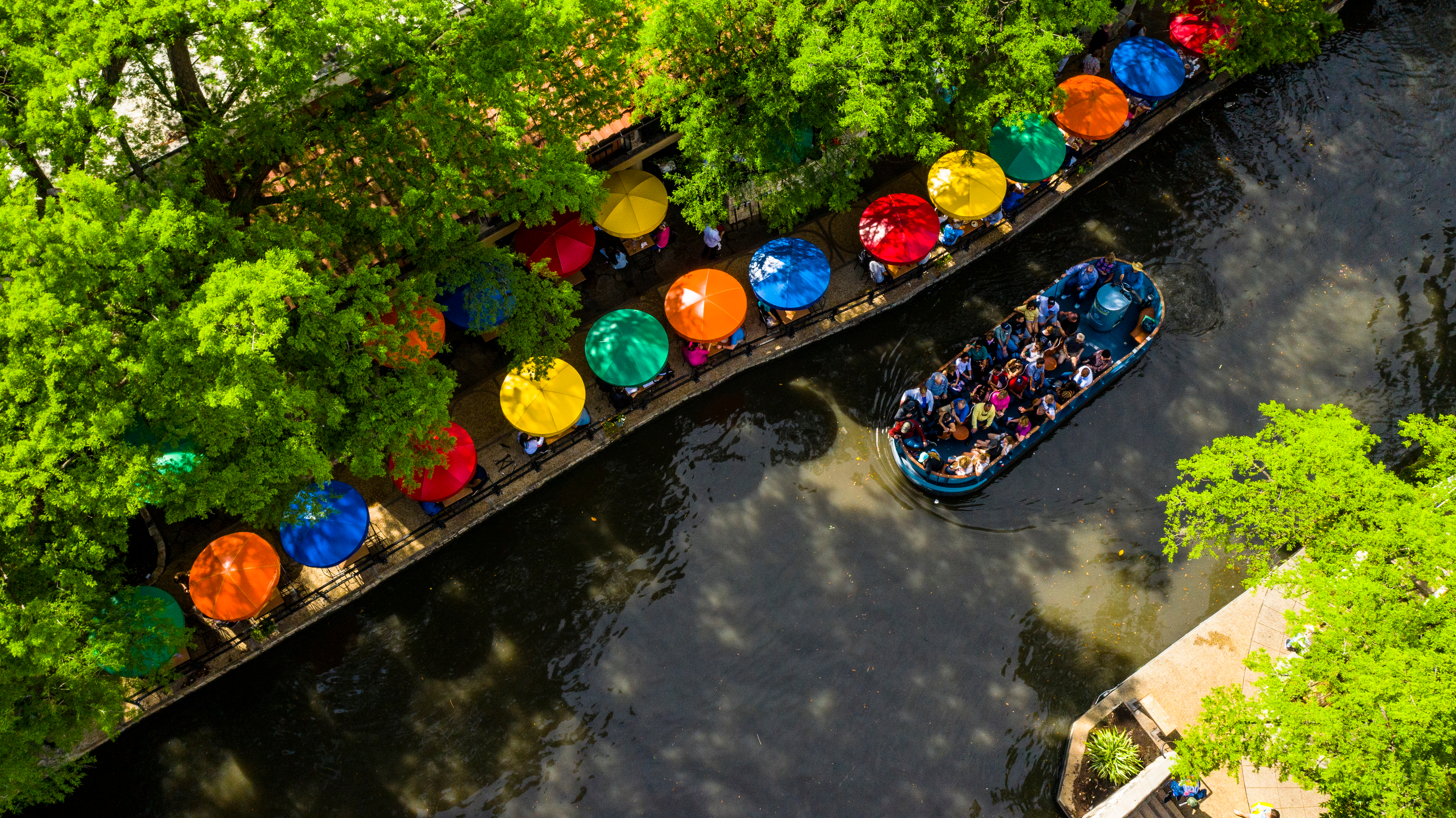 Aerial view of the San Antonio River Walk, with colorful umbrellas and a tour boat