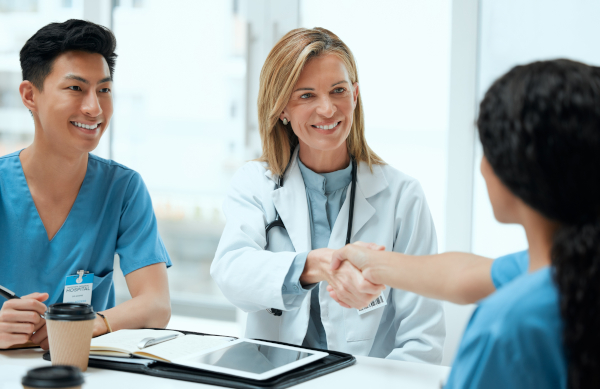 Hiring manager in a white coat shaking hands with a nurse across a table