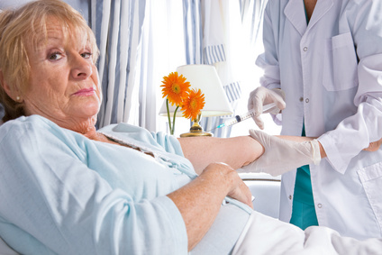 An older patient in a hospital bed winces as a clinician gives her an injection